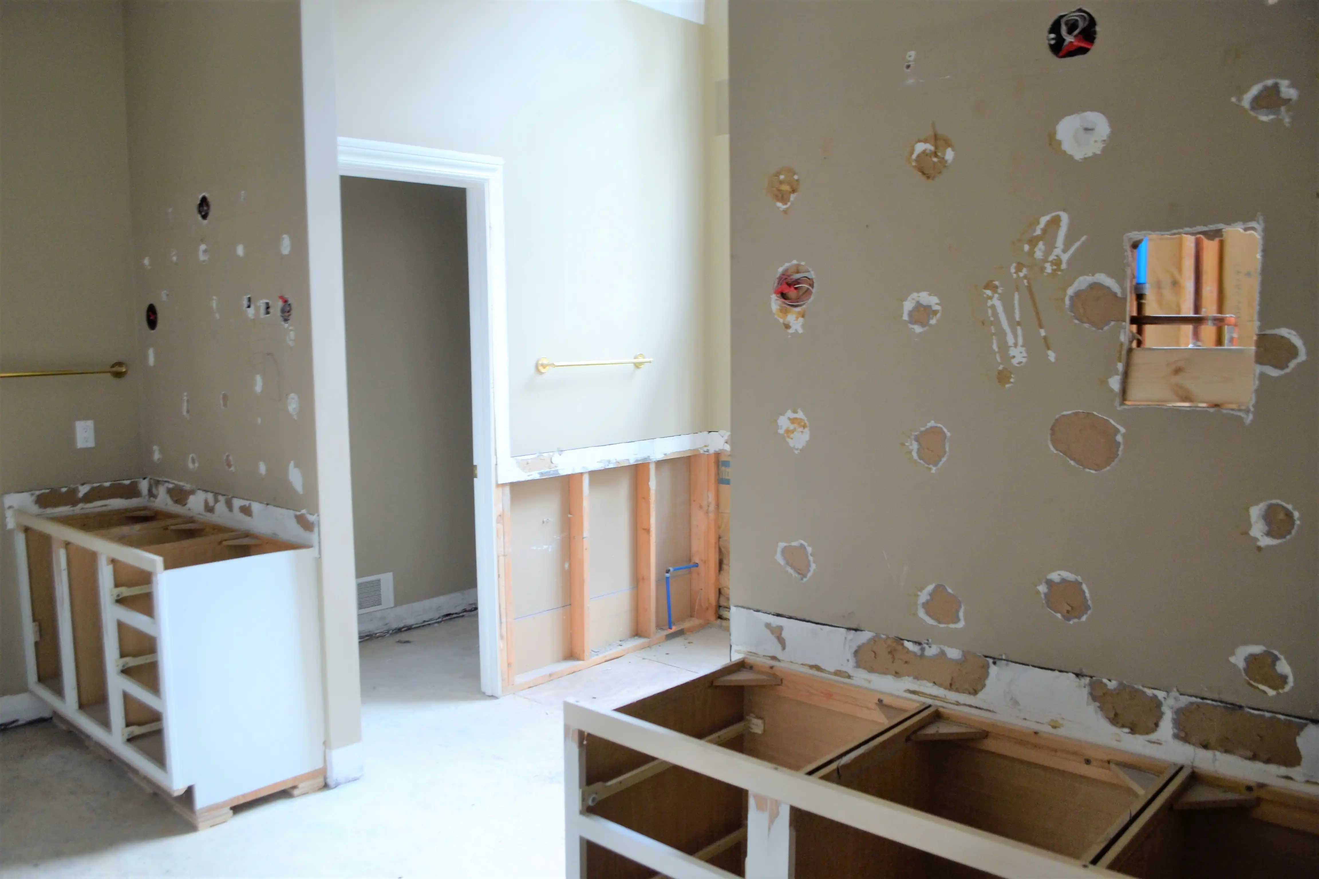 A kitchen mid-demolition with cabinets removed and walls opened up for plumbing and electrical work