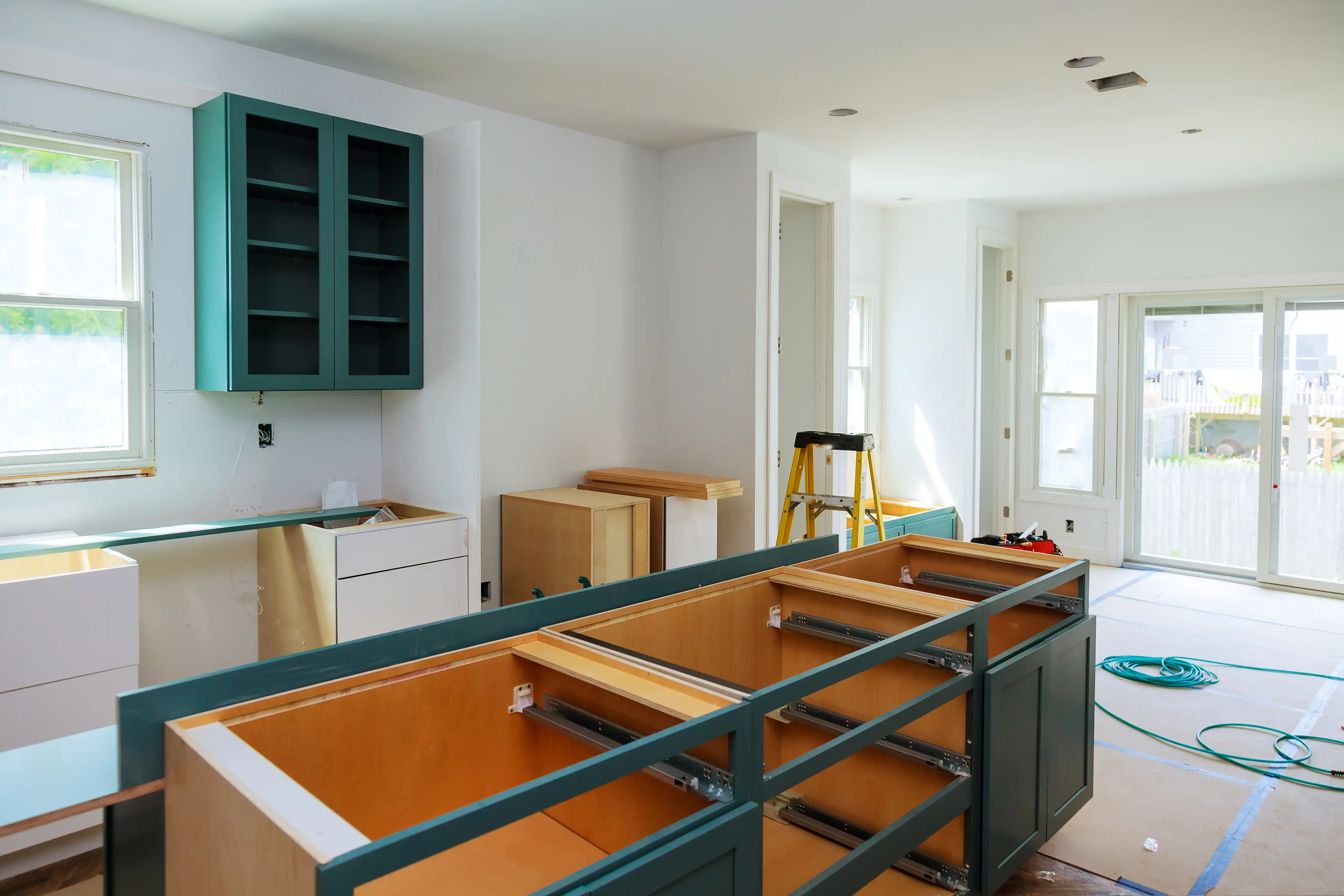 A kitchen renovation in progress with new green Shaker cabinets being installed by a contractor