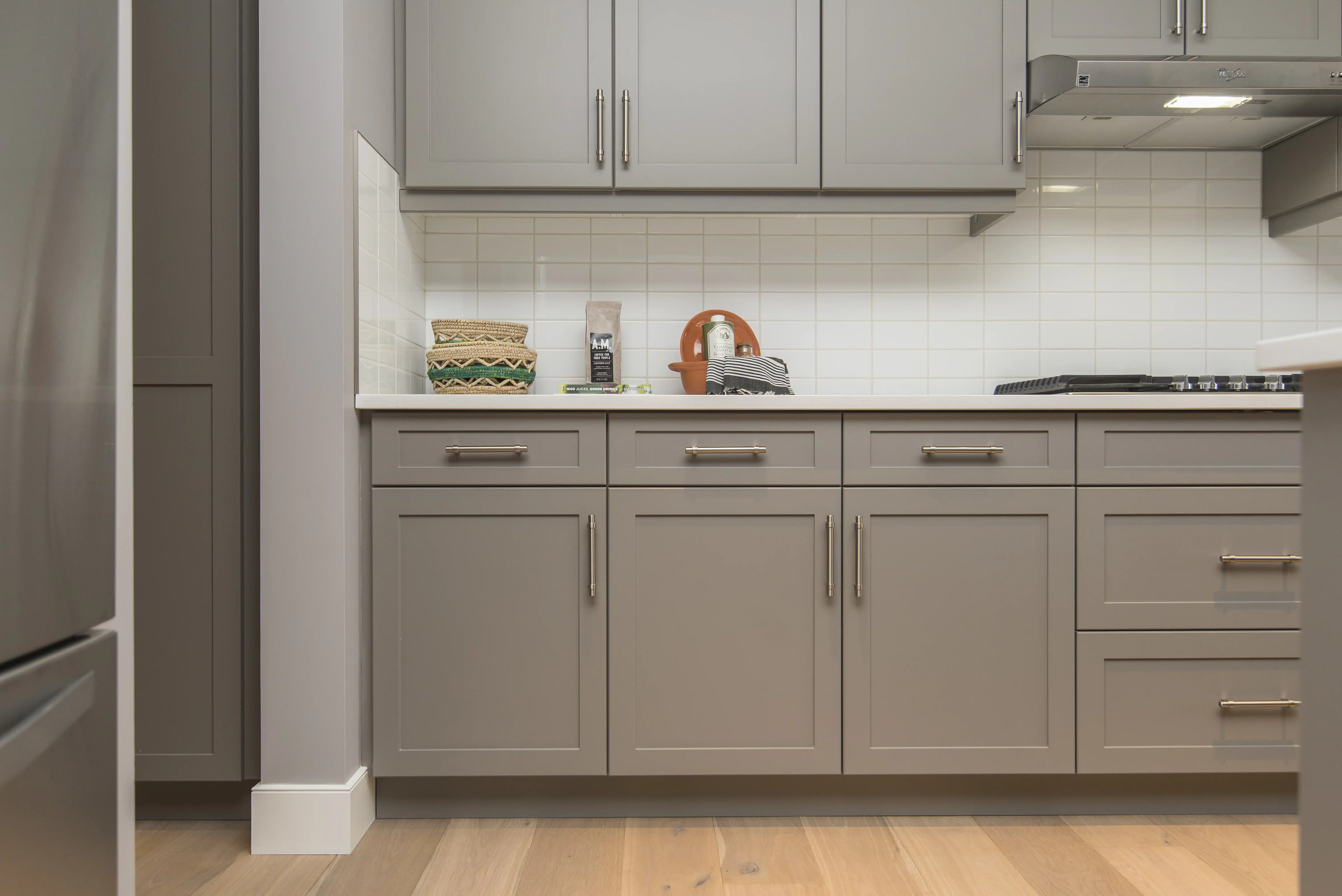 A modern kitchen with gray Shaker-style cabinets, white subway tile backsplash, and light hardwood floors