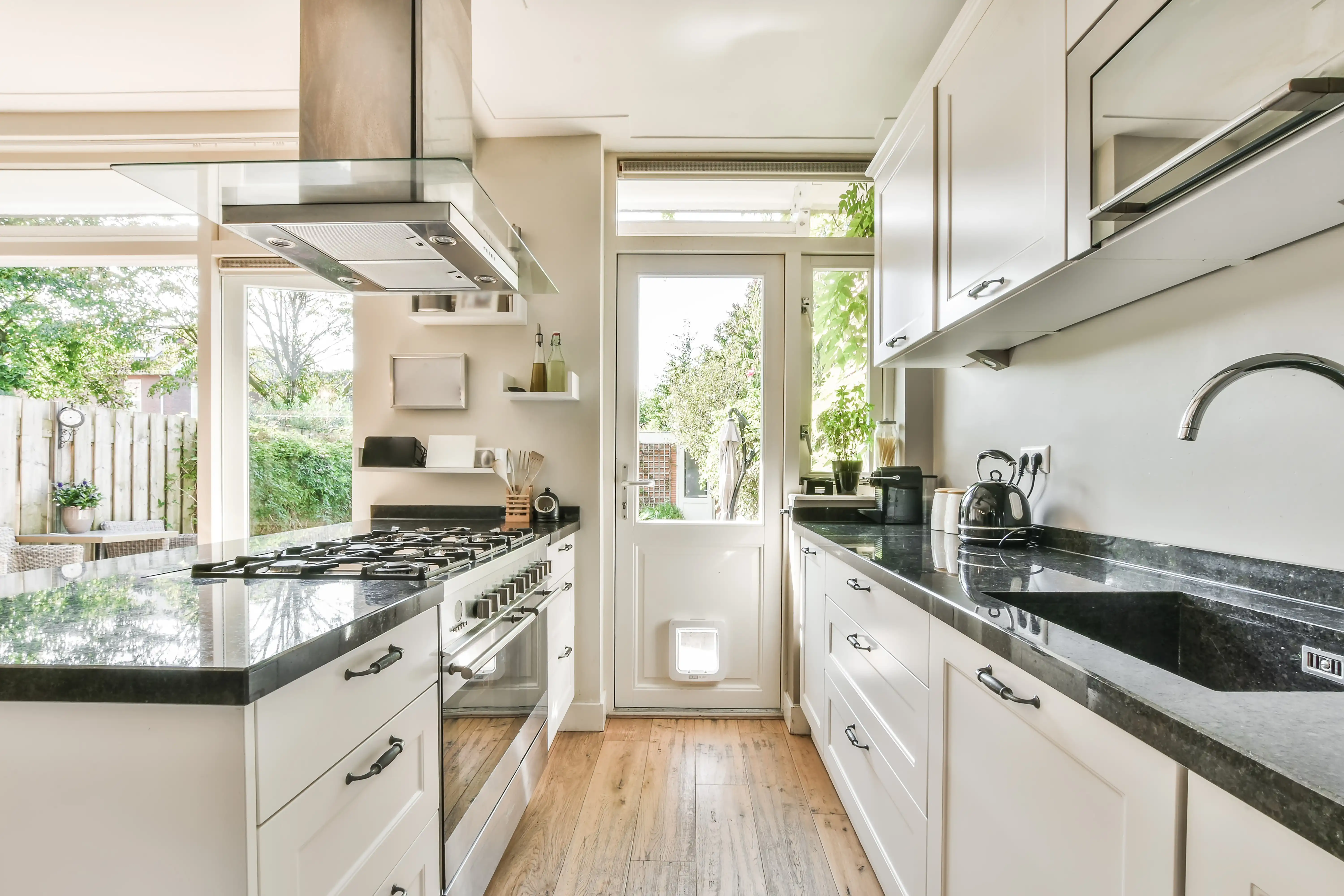 A bright kitchen with black granite countertops, white cabinets, and natural light from large windows