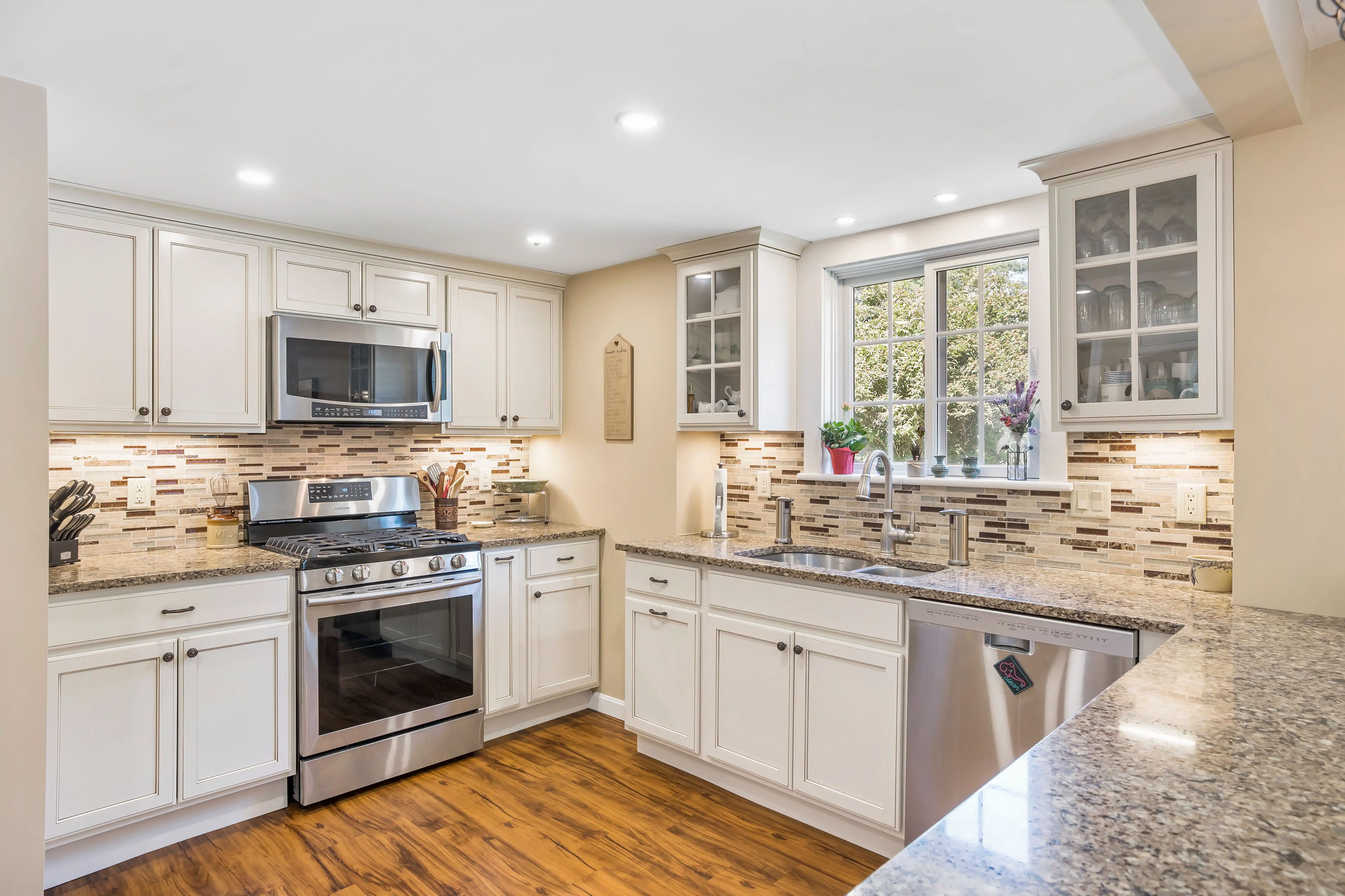 A finished traditional kitchen with white cabinets, granite countertops, stainless appliances, and tile backsplash